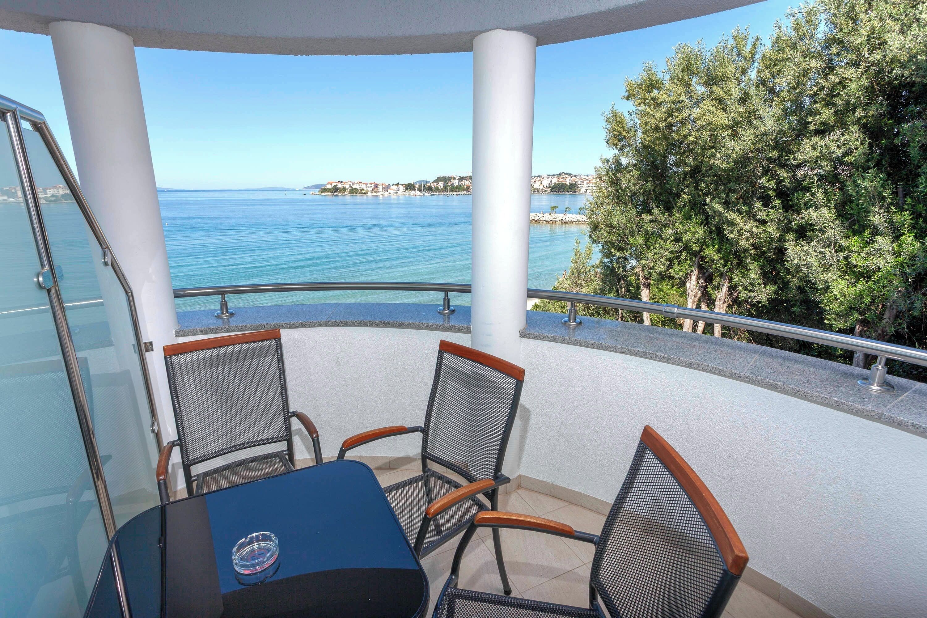 A balcony with a table and chairs, overlooking a body of water and a distant coastline.