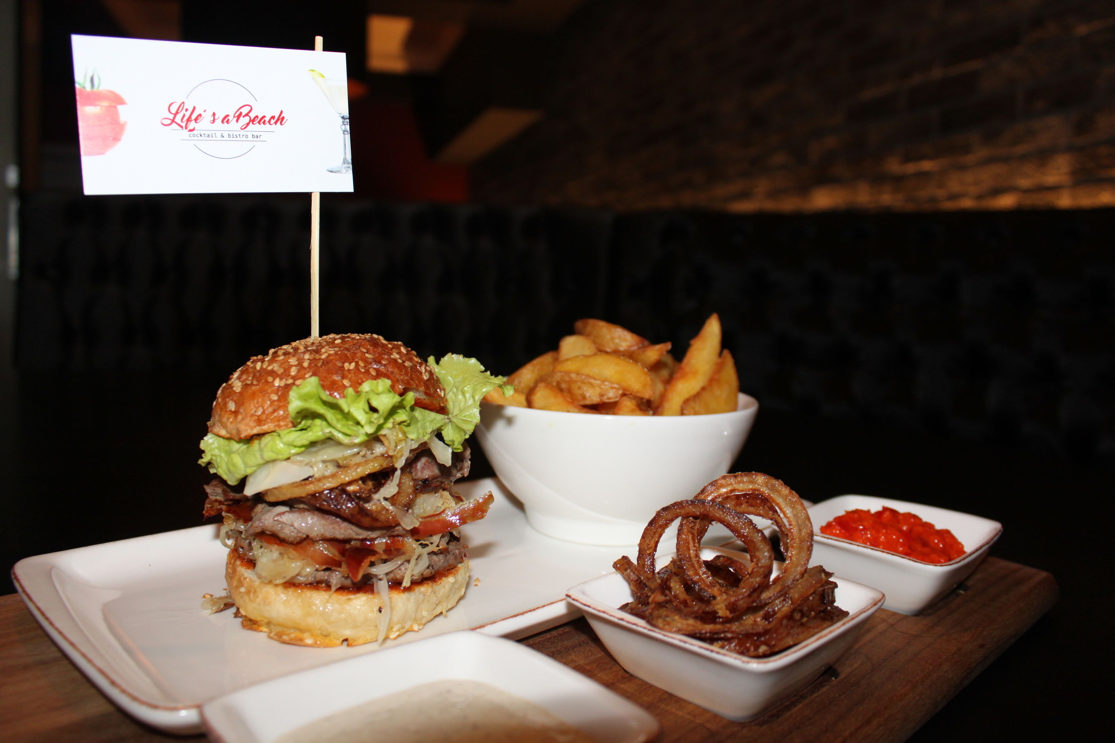 A burger with fries and onion rings on a wooden table.