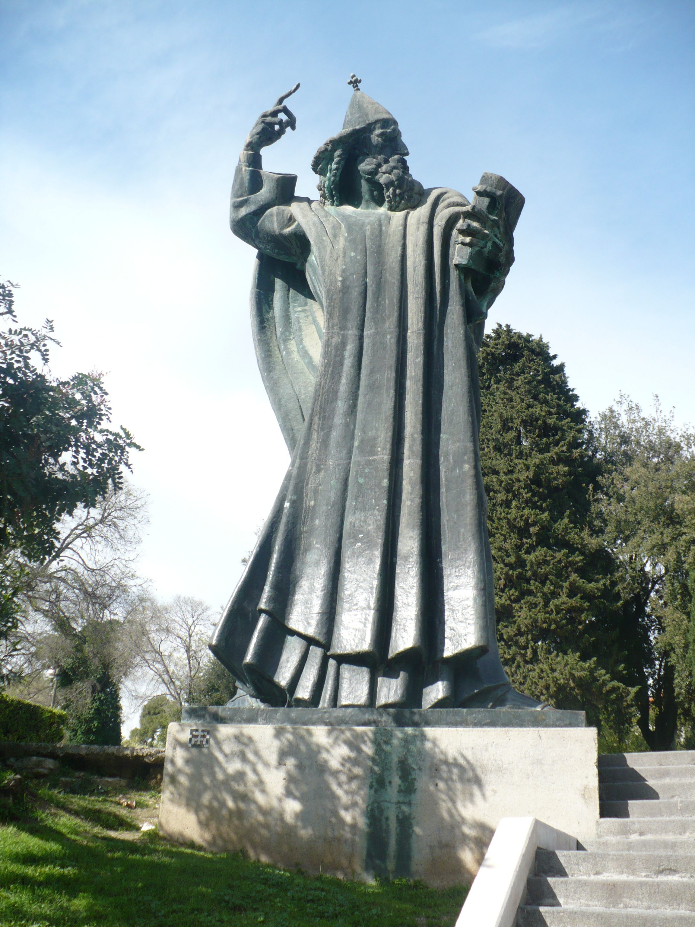 A statue of a figure in a robe holding a staff and a book, standing on a pedestal with stairs leading up to it.