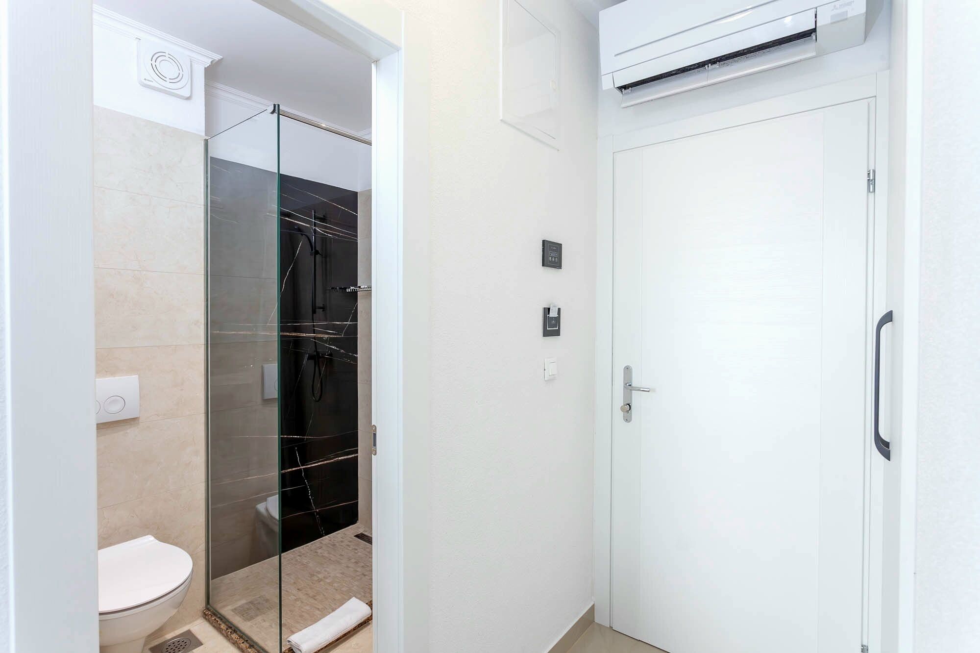 A bathroom with a glass-enclosed shower, a toilet, and a white door.