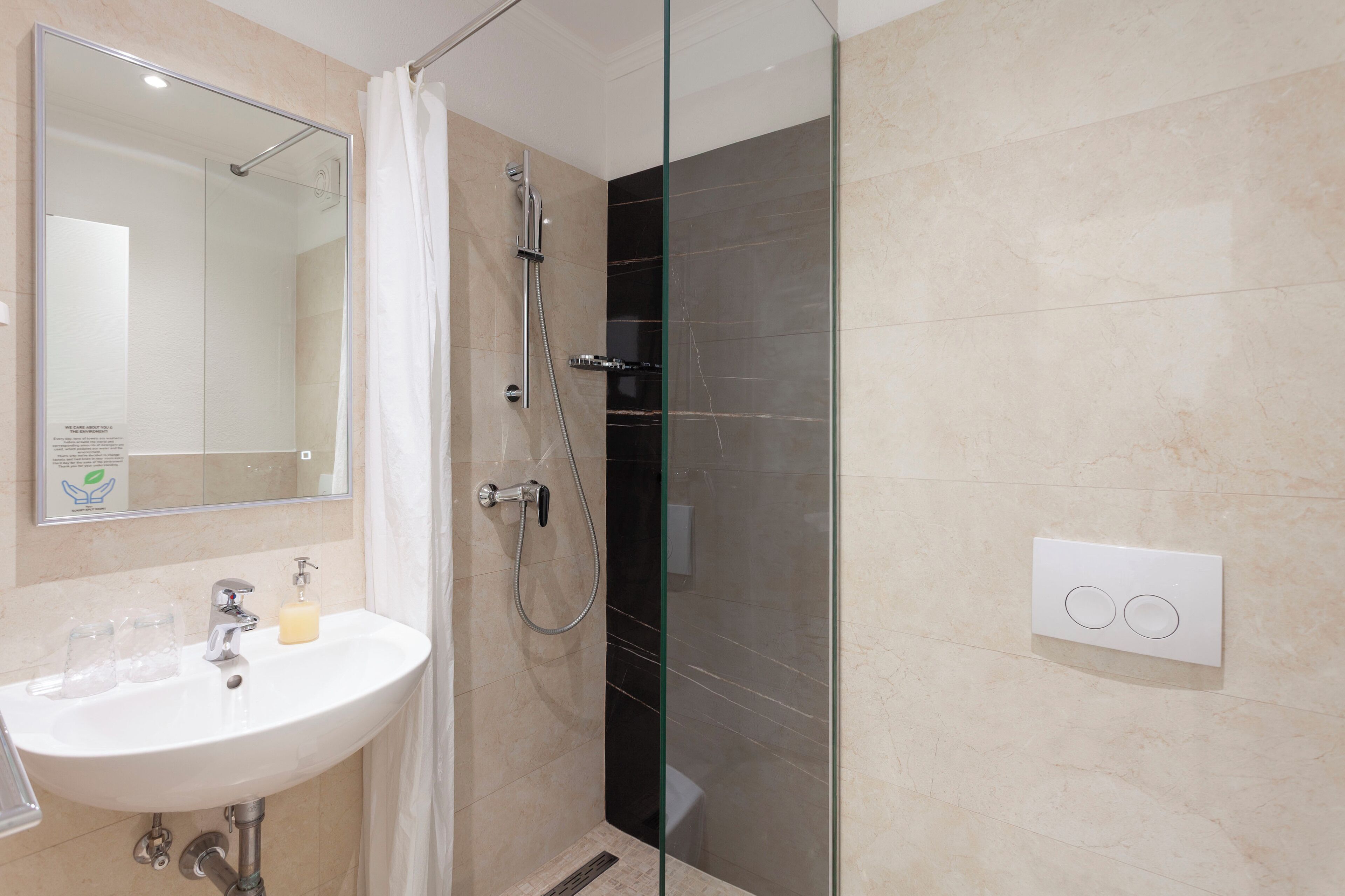 A modern bathroom with a glass-enclosed shower, a white sink with two glasses, and a soap dispenser.