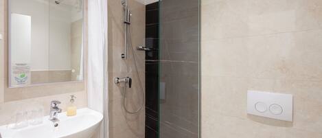 A modern bathroom with a glass-enclosed shower, a white sink with two glasses, and a soap dispenser.