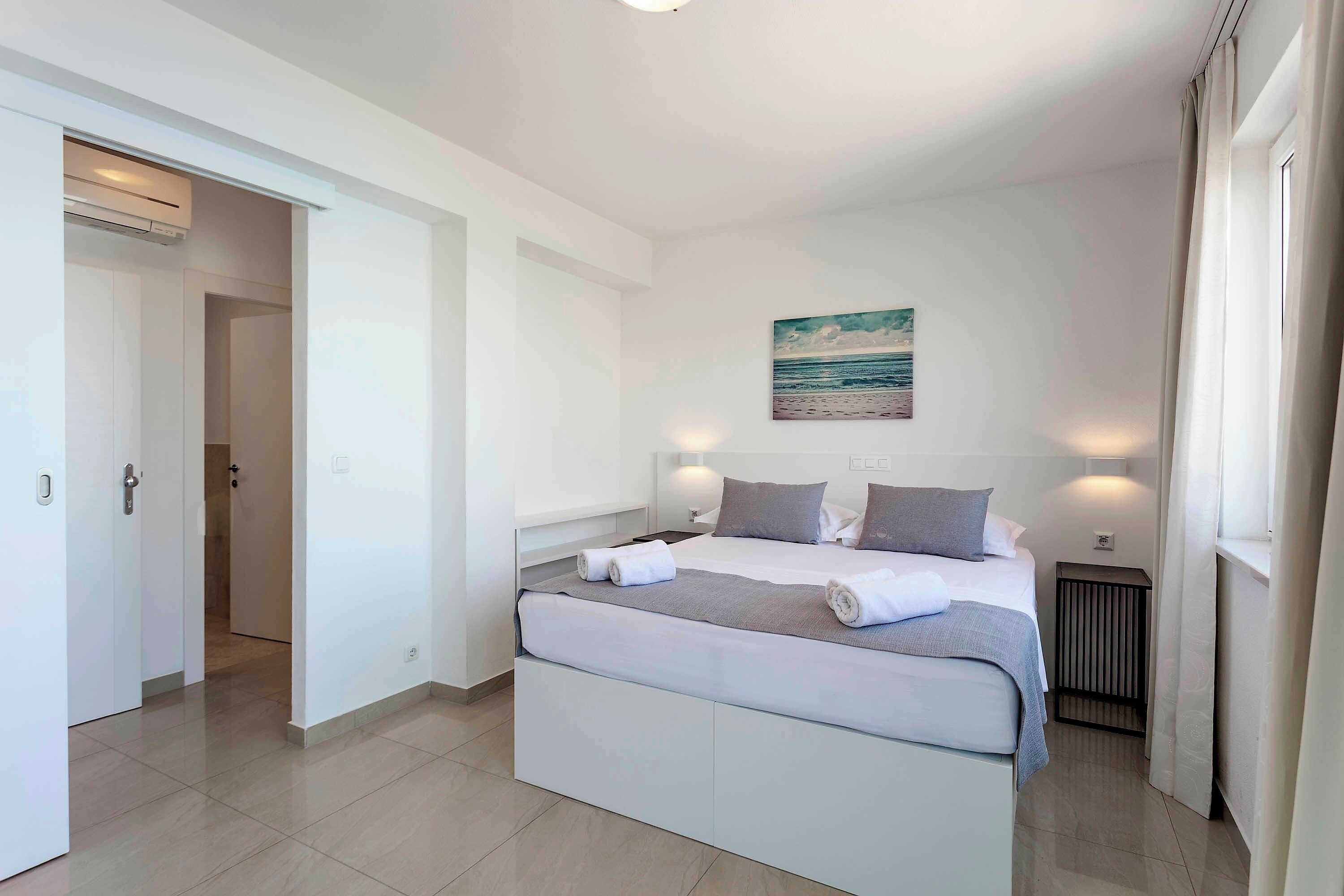 A modern bedroom with a large bed, a bedside table, a wall-mounted artwork, and a window with curtains.