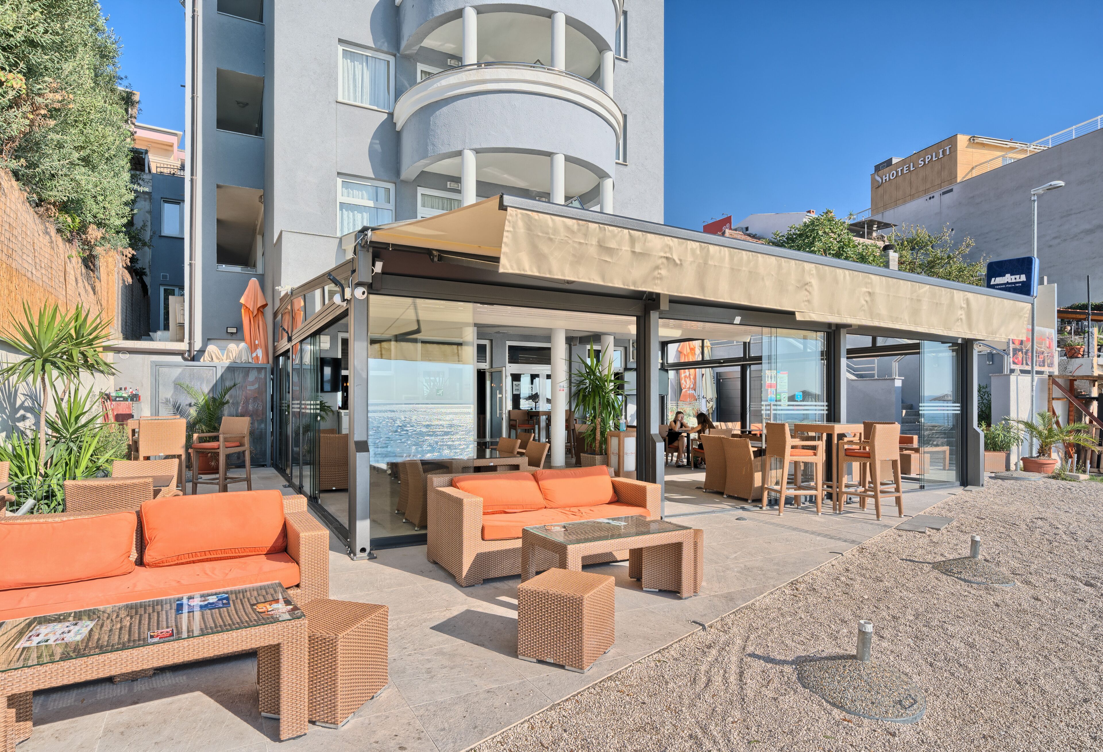 An outdoor seating area with wicker furniture and a glass table, overlooking a building with a balcony and a sign reading "HOTEL SPLIT".