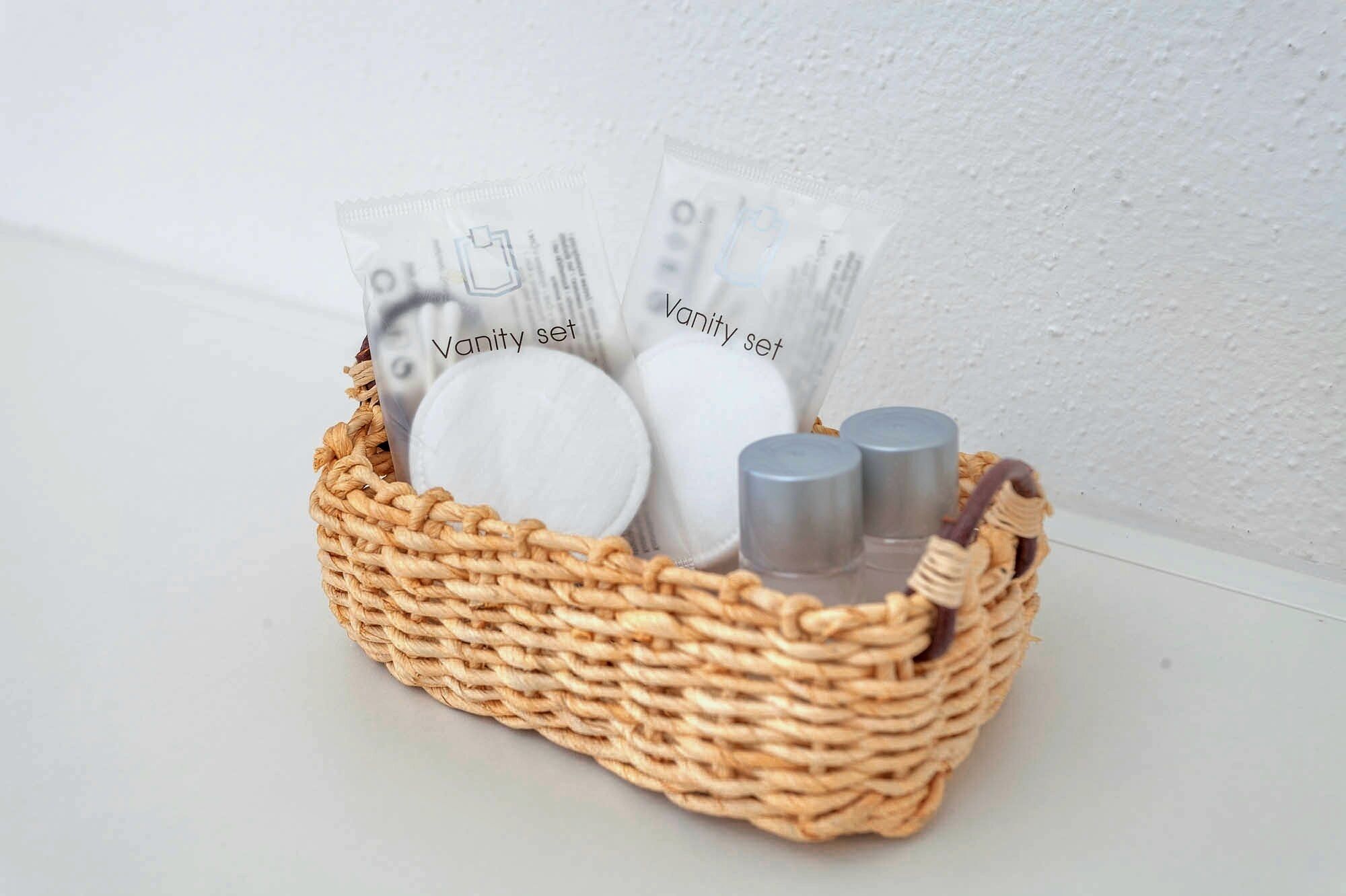 A wicker basket containing a vanity set with a mirror, two bottles, and two packets labeled "Vanity set".