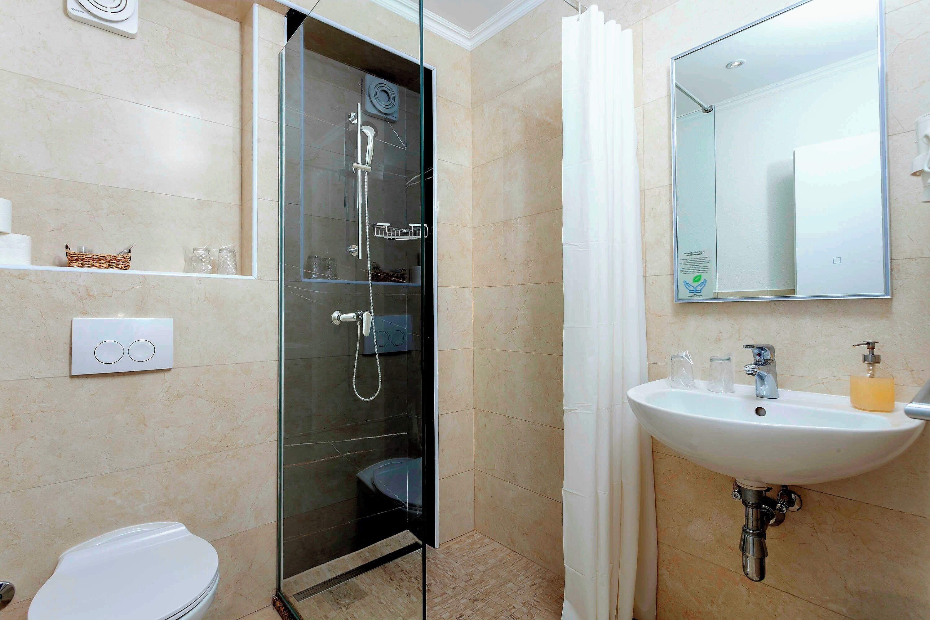 Uma casa de banho moderna com chuveiro envolto em vidro, lavatório branco com dispensador de sabão e sanita.