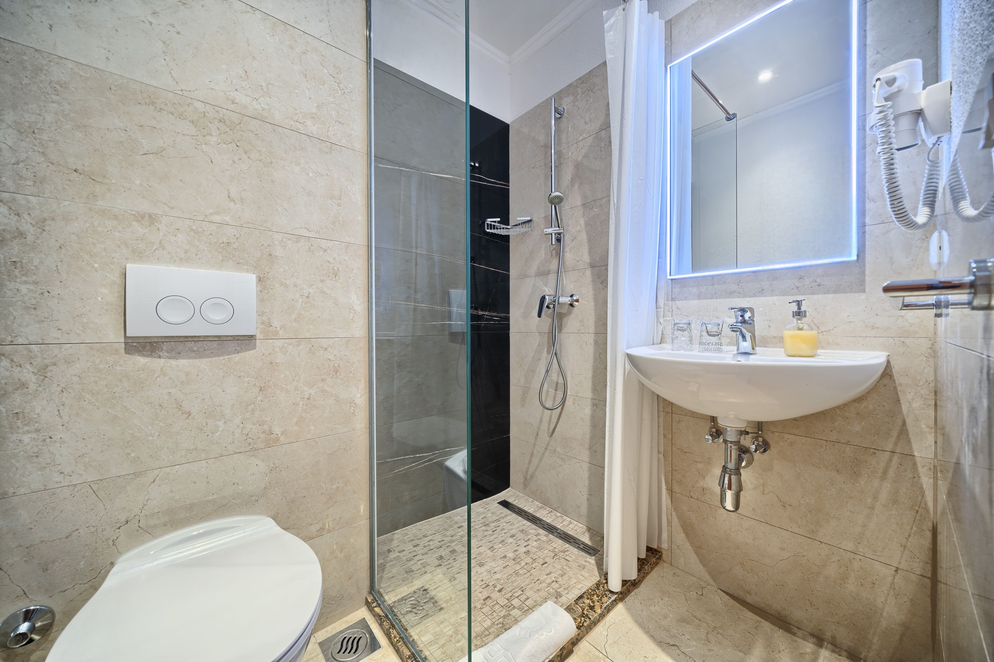 A modern bathroom with a glass-enclosed shower, a white toilet, and a sink with a soap dispenser.