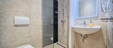 A modern bathroom with a glass-enclosed shower, a white toilet, and a sink with a soap dispenser.