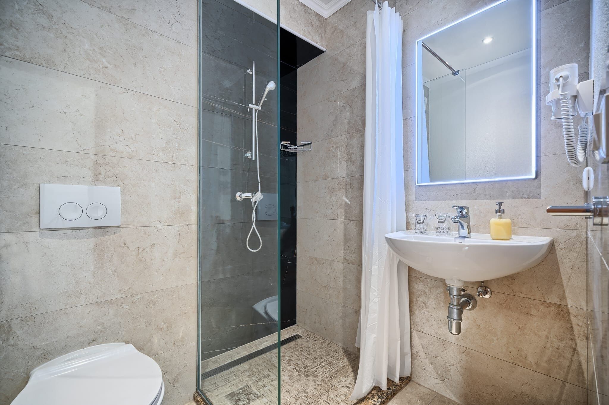 A modern bathroom with a glass-enclosed shower, a white sink with a soap dispenser, and a mirror above the sink.