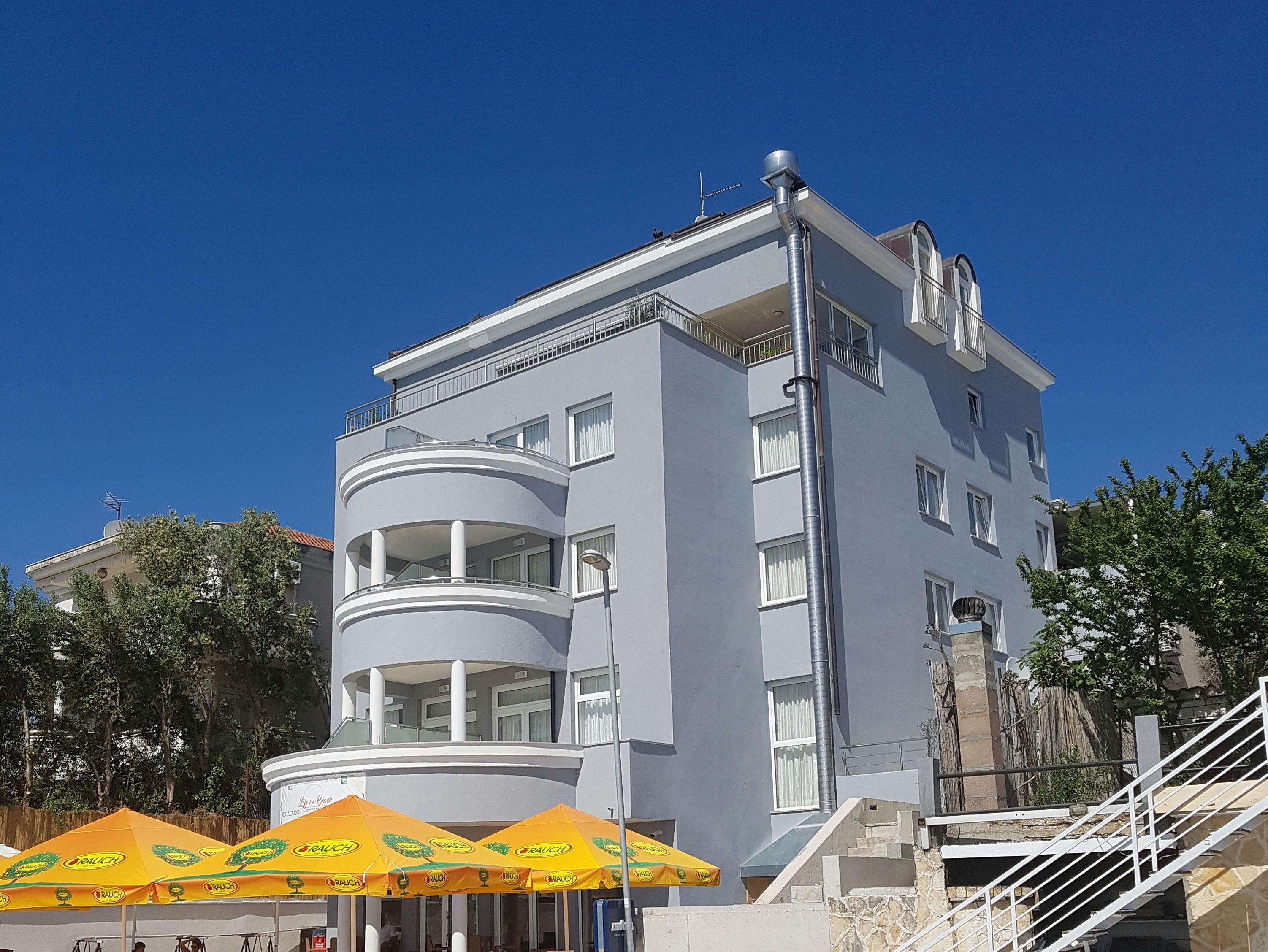 Un edificio de varios pisos con balcones, una escalera y mobiliario exterior con sombrillas amarillas.