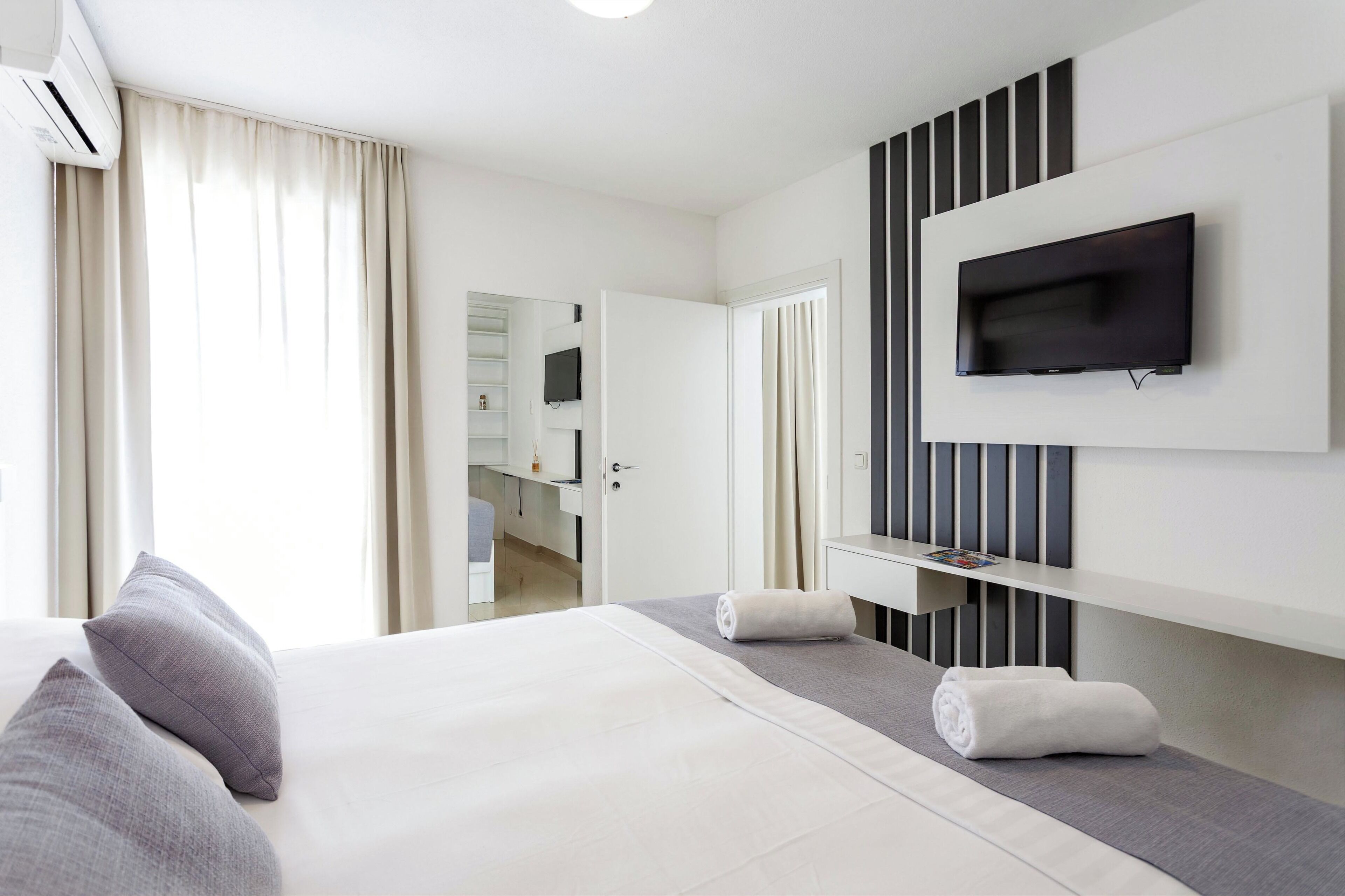 Une chambre d’hôtel moderne dotée d’un grand lit, d’un téléviseur à écran plat fixé au mur, d’un petit bureau et d’un dressing.