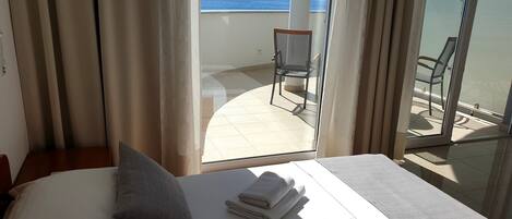 Une chambre d’hôtel avec un lit, des oreillers et une vue sur la mer, visible à travers une porte vitrée.