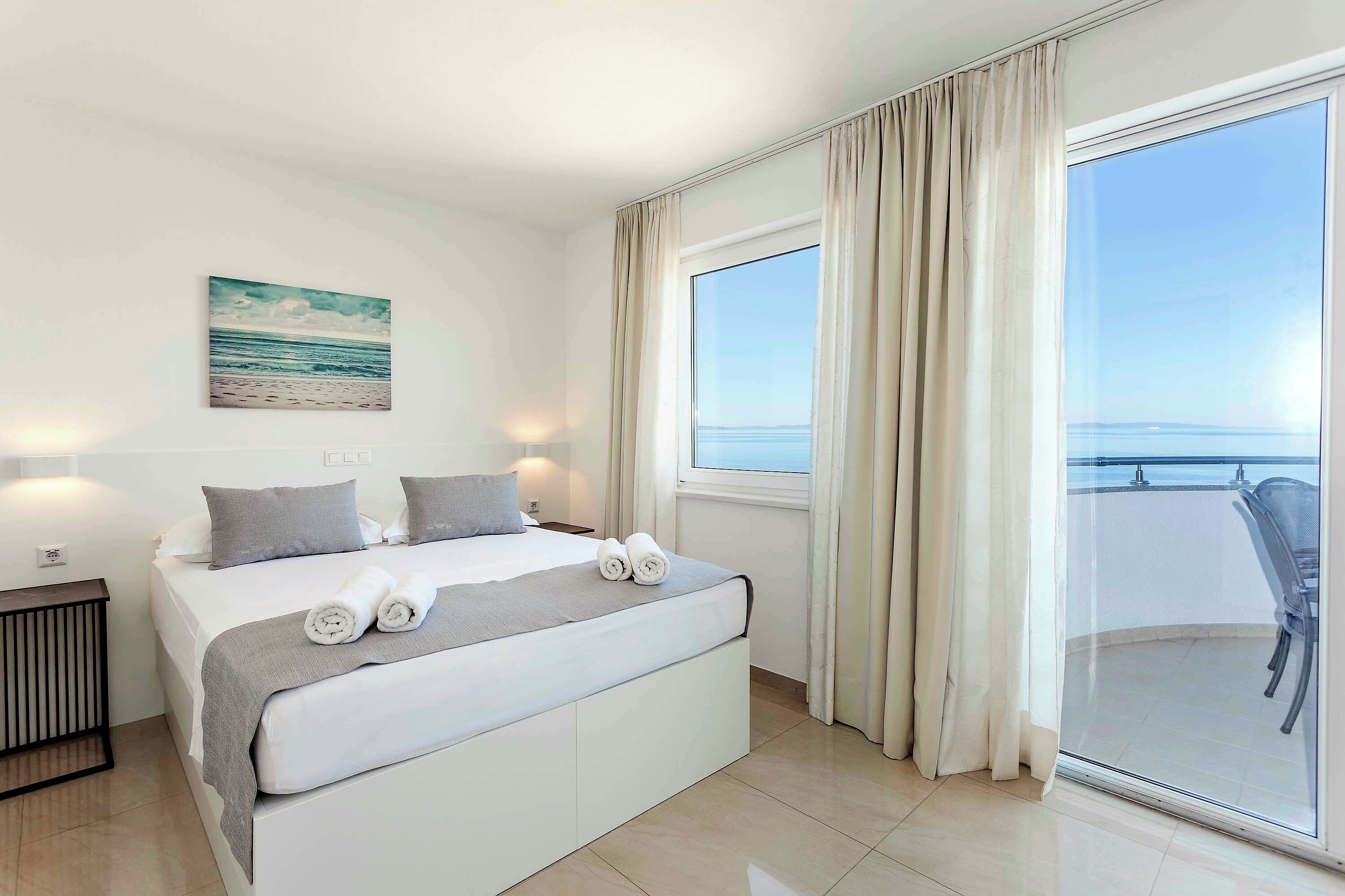 A hotel room with a bed, a bedside table, a window with curtains, and a view of the sea.