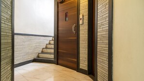 Un pasillo con piso de mármol, una puerta de madera con picaporte y una pequeña pantalla digital.