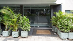 Una entrada moderna de edificio con puerta de cristal, plantas en macetas y un camino empedrado.