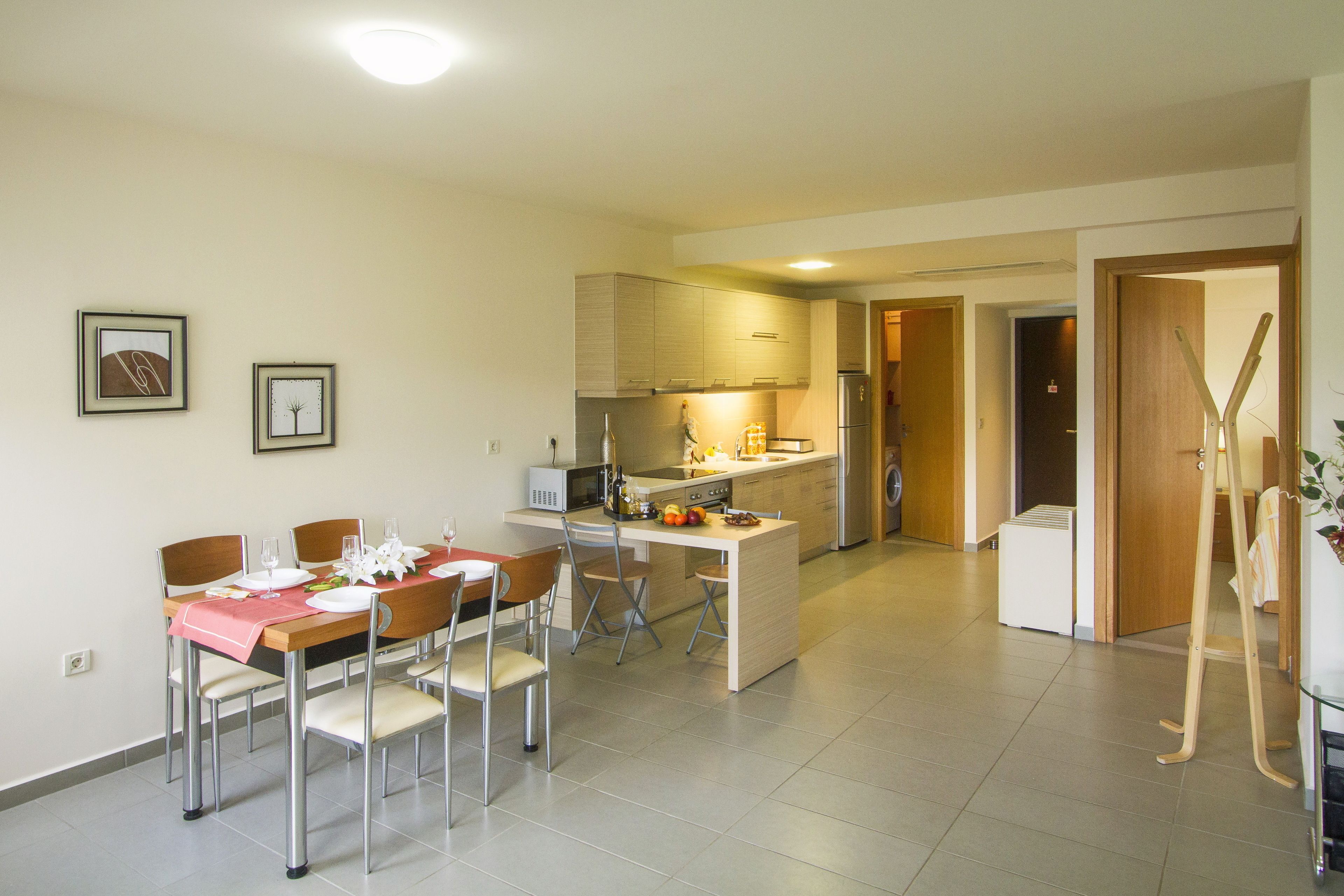 A modern kitchen with a dining area, featuring a central island, stainless steel appliances, and a wooden table set for four.