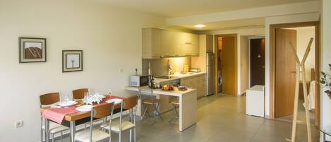 A modern kitchen with a dining area, featuring a central island, stainless steel appliances, and a wooden table set for four.