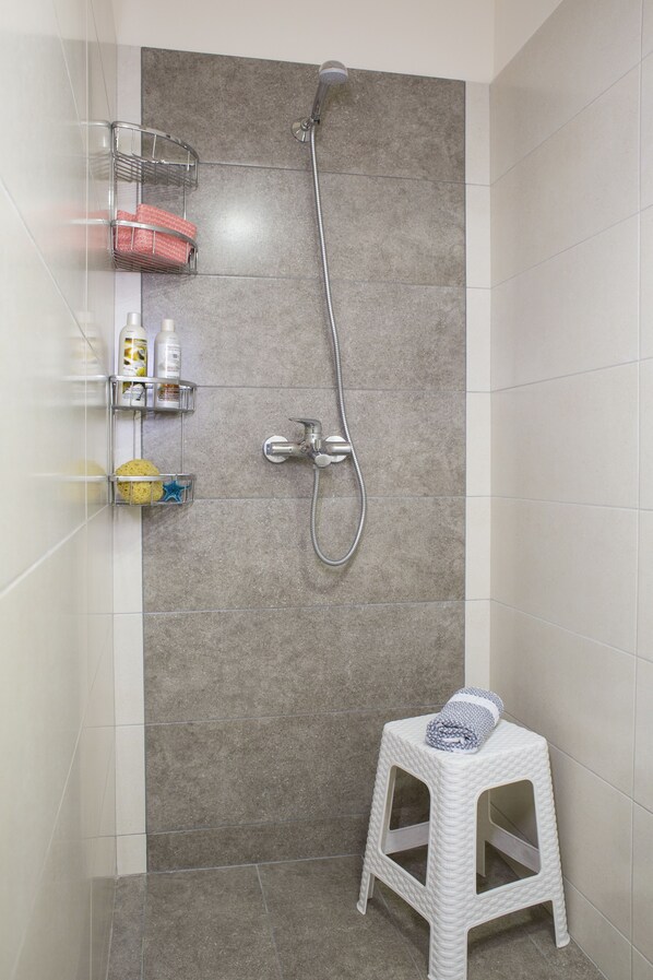 A shower area with a handheld showerhead, a small stool, and storage shelves with toiletries.