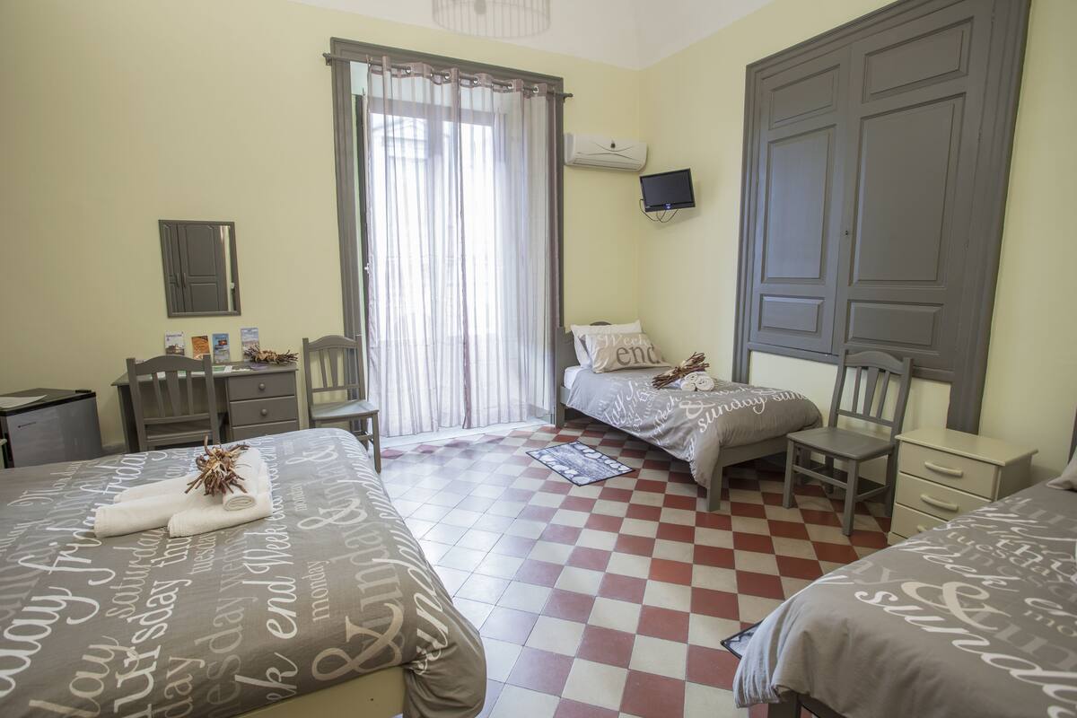 A hotel room with two beds, a desk, a chair, a television, and a window with curtains.
