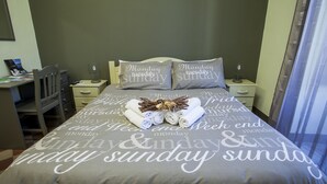 A neatly made bed with rolled towels and a decorative centerpiece, a desk with a chair, and a nightstand with a lamp and a small table. - Sicilia Etna Mare (Riposto)