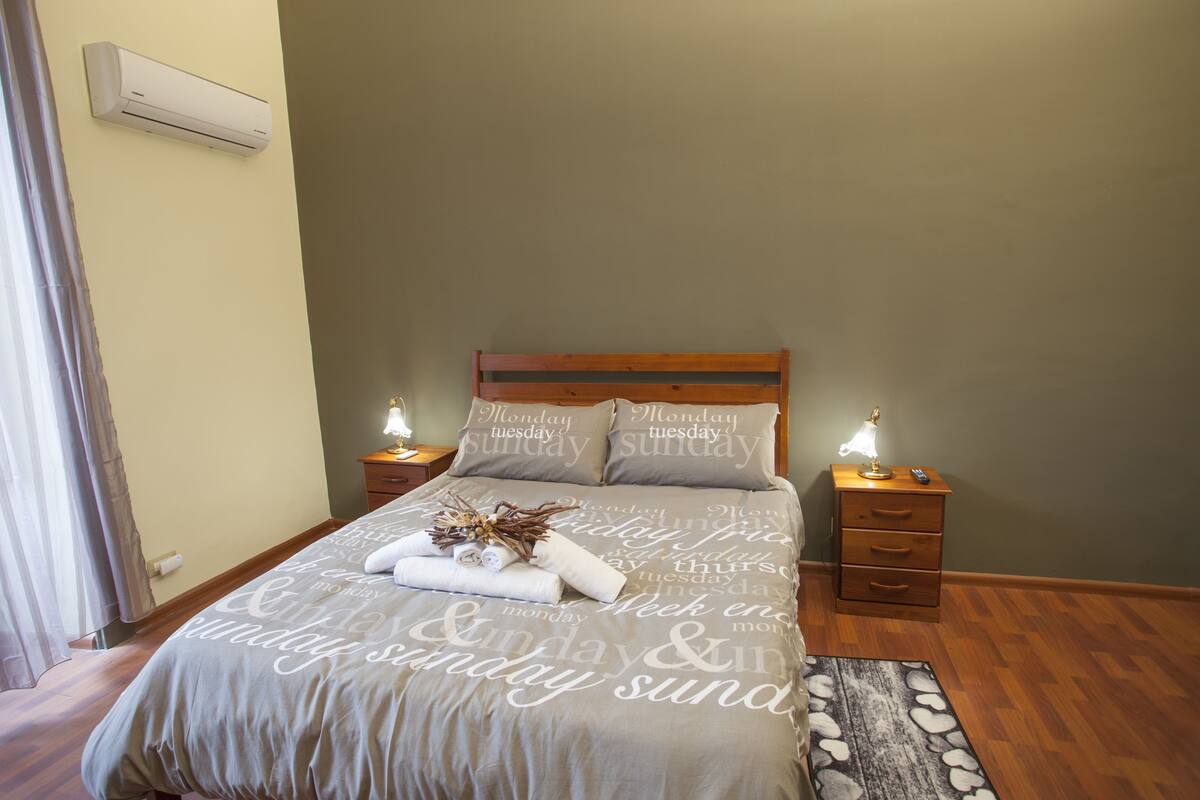 A neatly made bed with a grey bedspread and pillows, two bedside tables with lamps, and a wooden headboard.