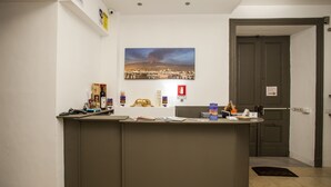 A reception desk with a cityscape painting above it, a fire extinguisher, and a door to the right. - Sicilia Etna Mare (Riposto)