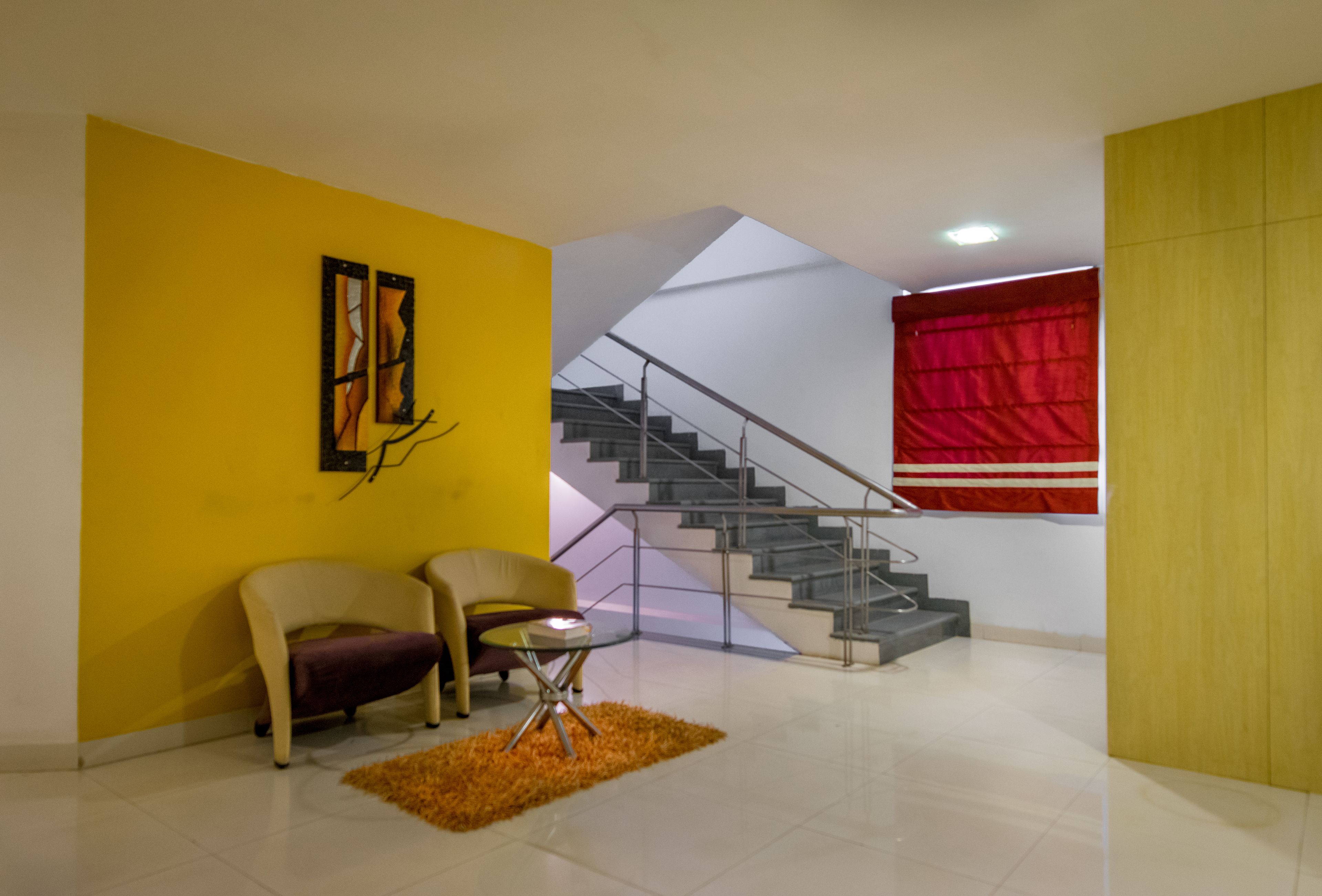 A modern living room with a yellow accent wall, a staircase, and a red curtain.