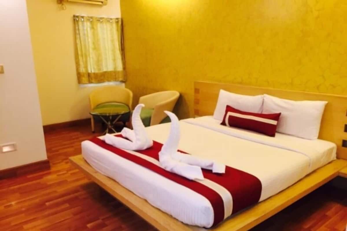 Una habitación de hotel con cama, una silla, una mesita y una cortina.