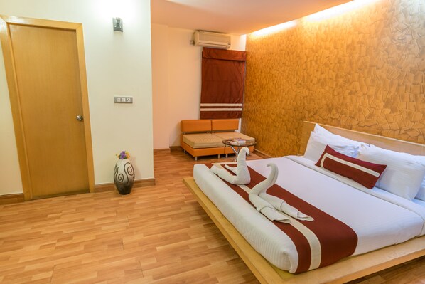 A hotel room with a wooden floor, a bed with white and red bedding, a small sofa, and a decorative vase. - Octave Hotel & Spa Marathahalli (Bengaluru)