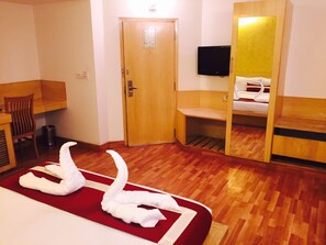 A hotel room with a wooden floor, a bed with white linens, a wooden desk, a chair, a television, and a mirror. - Octave Hotel & Spa Marathahalli (Bengaluru)