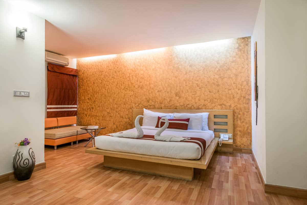 Una habitación de hotel moderna con suelo de madera, una cama con cabecero de madera, una mesita pequeña, un banco y una pared con un diseño texturizado.