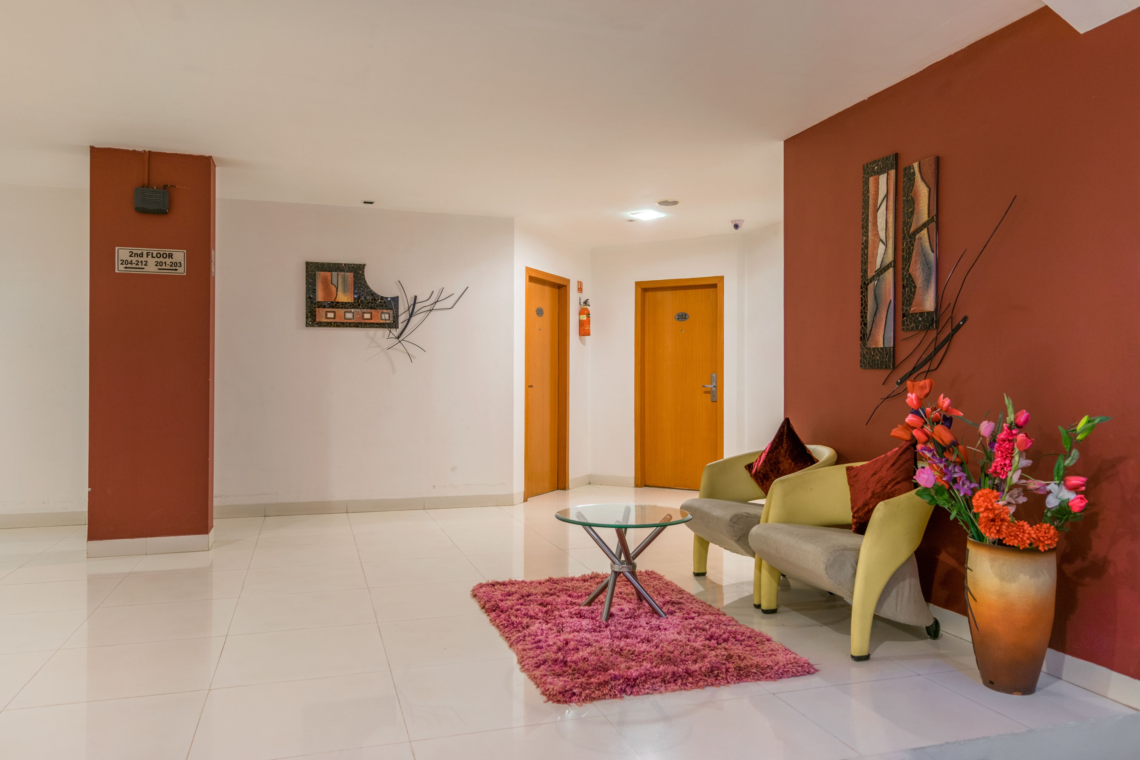 A modern lobby with a sofa, a glass coffee table, a pink rug, and a vase of flowers.