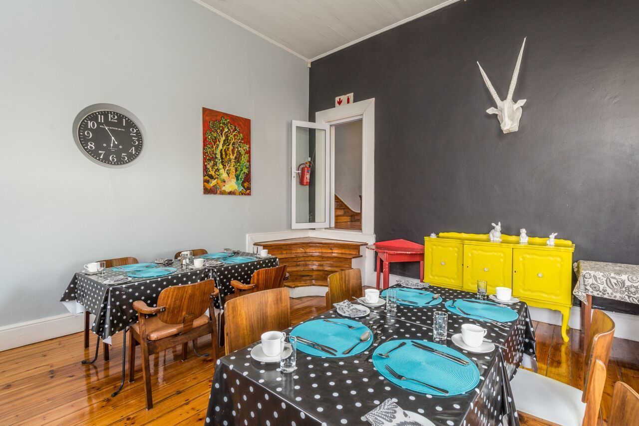 Un coin repas avec des tables dressées pour quatre personnes, des chaises en bois, une horloge au mur et un tableau coloré.