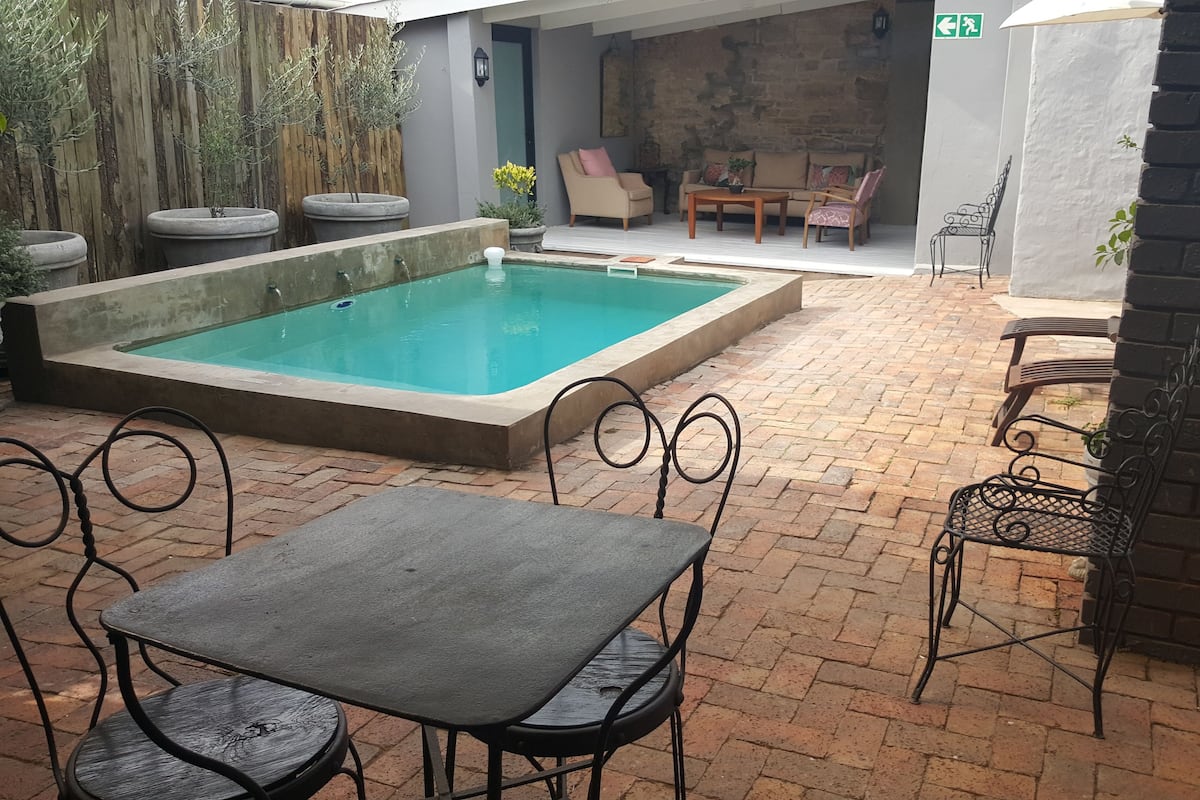 A pool area with a rectangular pool, outdoor seating, and a brick patio.