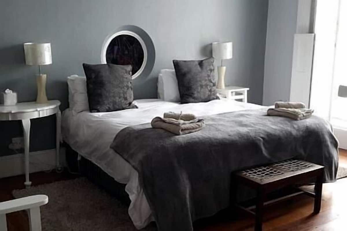 A neatly made bed with pillows, a bedside table with a lamp, and a bench in a modern bedroom.