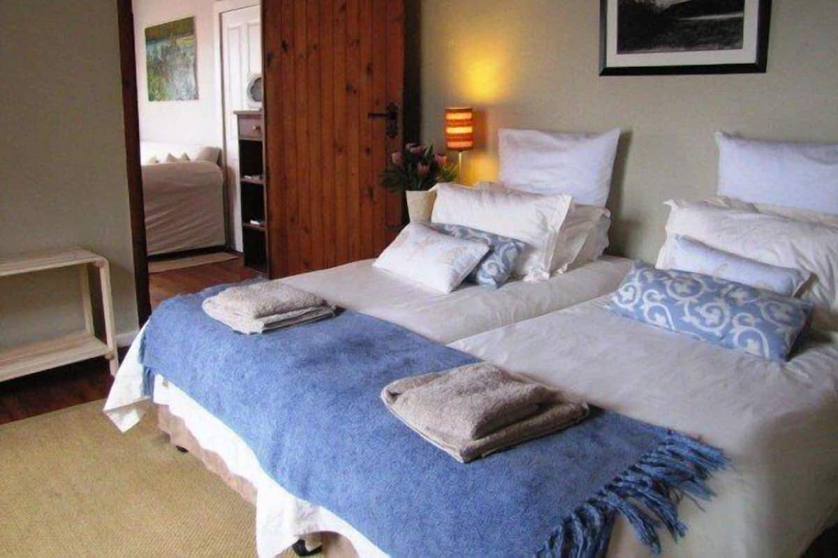 A bedroom with two beds, a wooden door, a bedside lamp, and a framed picture on the wall.