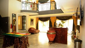 A spacious living area with a high ceiling, a balcony, a large wooden table, and a large vase. - Mount Pleasant Inns & Apartment (Obosomase)