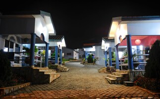 Vista noturna de um hotel, com um caminho de pedras que leva à entrada.