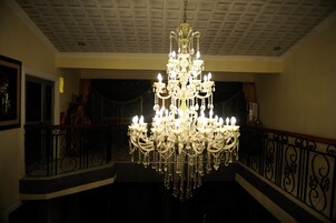 Um lustre imponente em um salão amplo, com teto alto e grades ricamente decoradas.