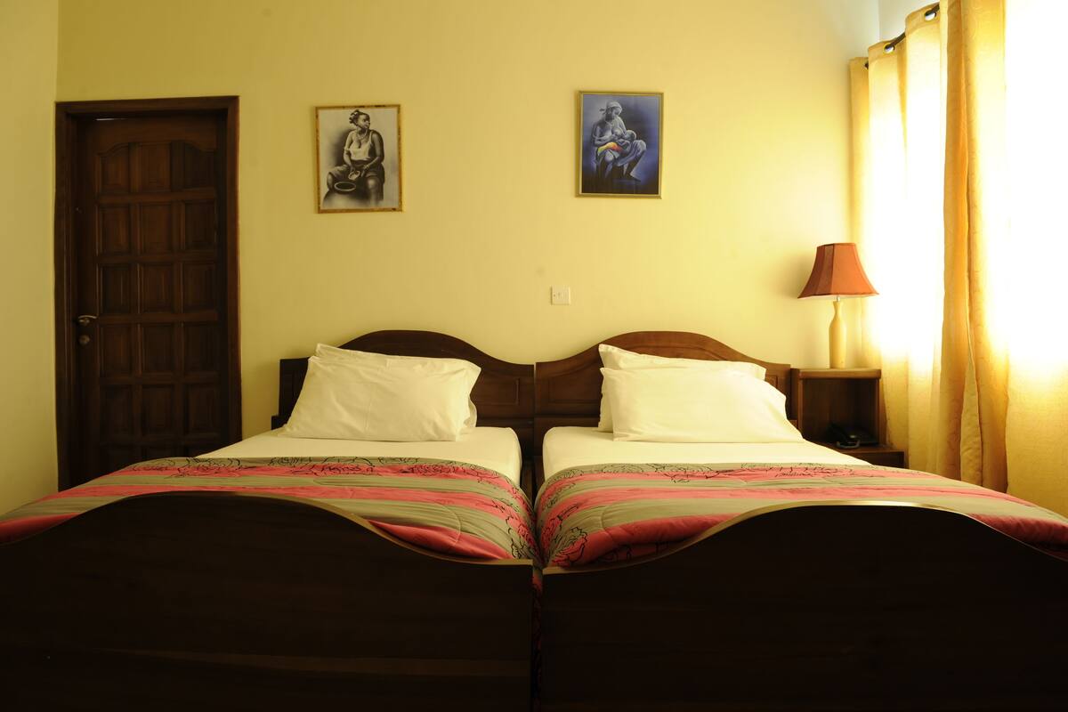 Une pièce avec deux lits, une porte en bois et deux tableaux encadrés accrochés au mur.