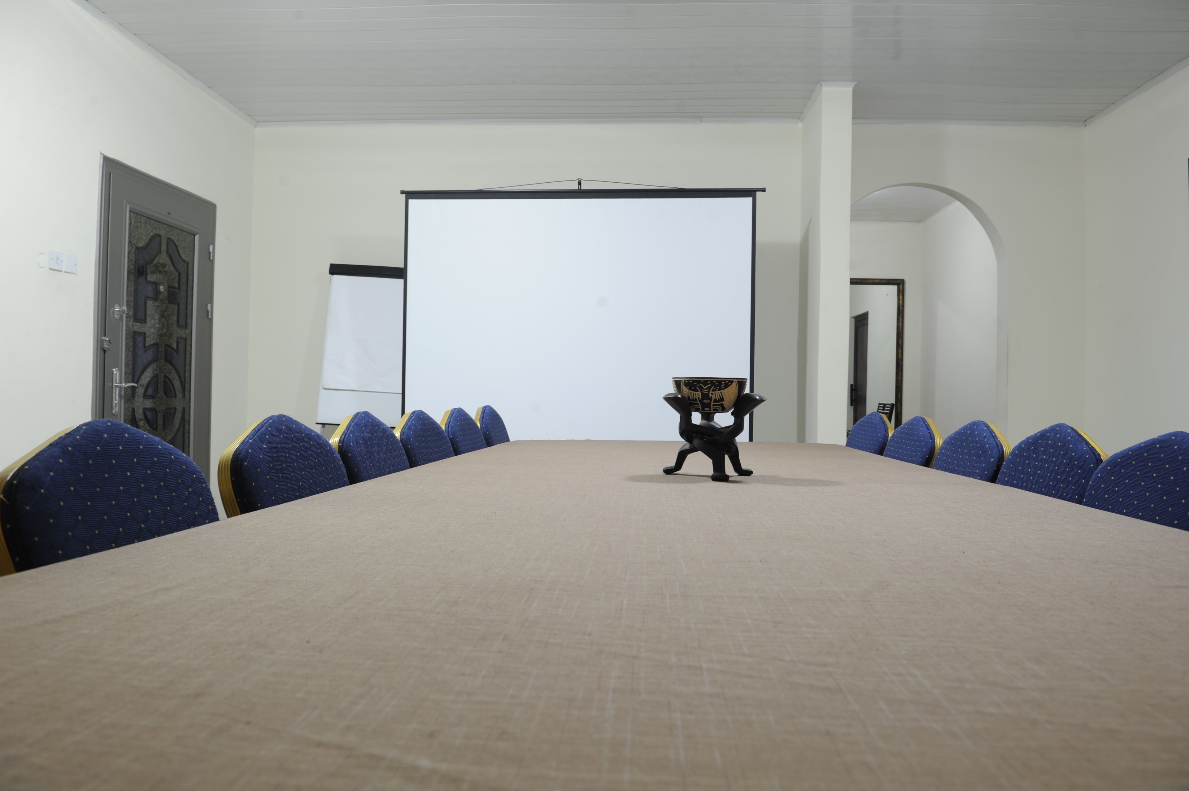 A conference room with a long table, blue chairs, a projector screen, and a door with a decorative design.