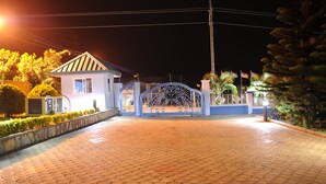 A gated entrance with a metal gate, a paved driveway, and a building with a sloped roof. - Mount Pleasant Inns & Apartment (Obosomase)