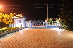 Uma entrada murada com portão de metal, um caminho de acesso pavimentado e um edifício com telhado inclinado.