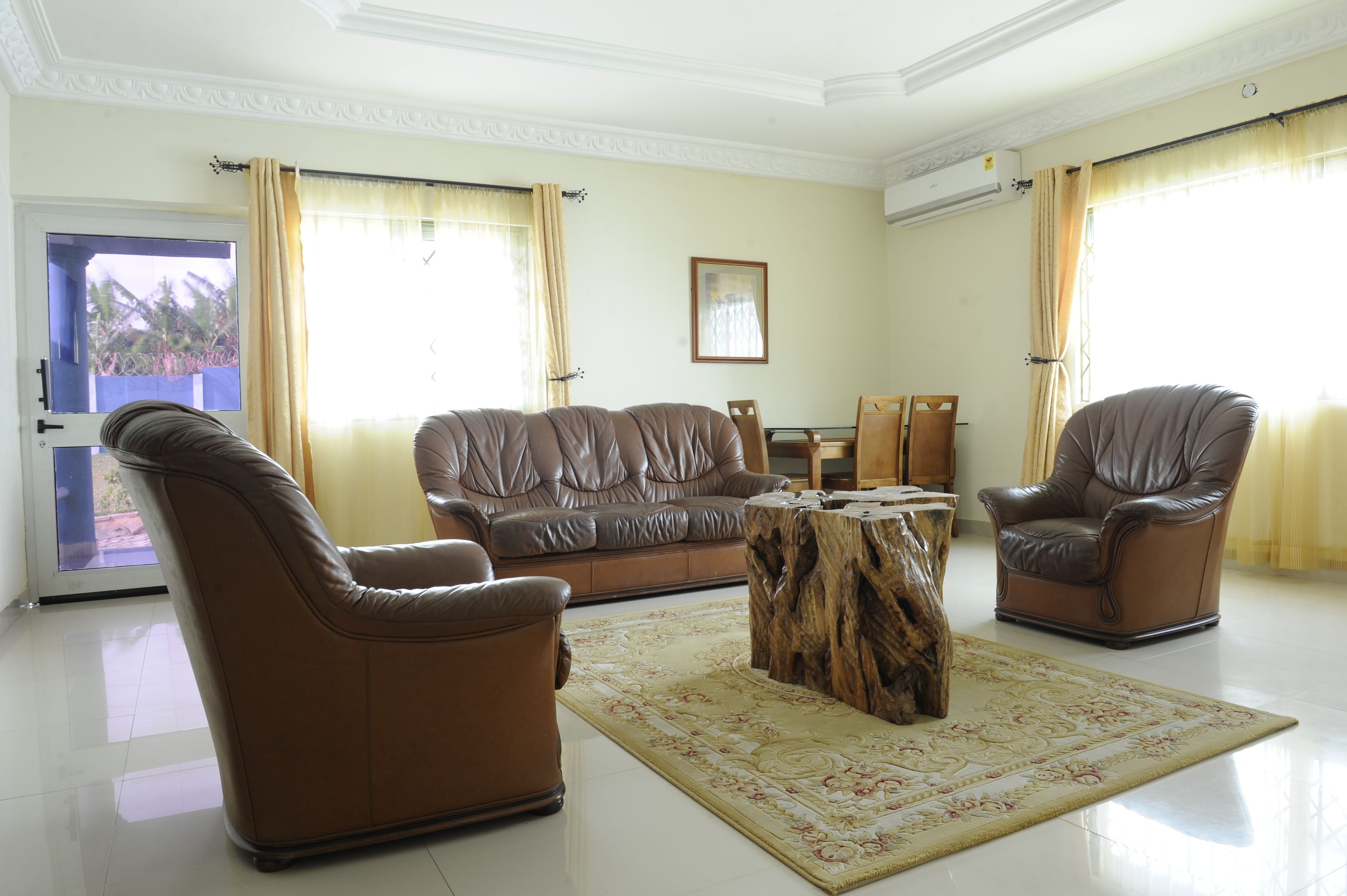 A living room with a brown leather sofa, two leather armchairs, a wooden coffee table, and a patterned rug.