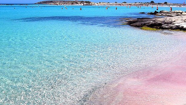 A beach with clear turquoise water, a rocky shoreline, and a distant hill. - Greta Apartments (Hersonissos)