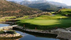 A golf course with a pond, stone walls, and a mountainous backdrop. - Greta Apartments (Hersonissos)
