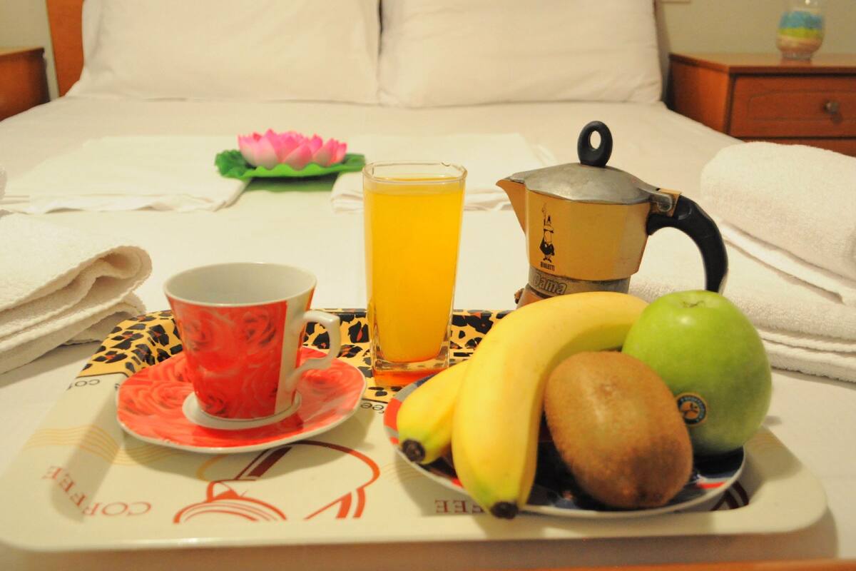 A breakfast tray with a cup, a glass of orange juice, a pot, and fruits on a bed.