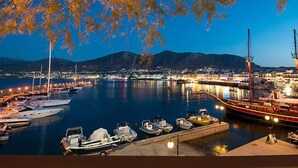 A marina at night with boats docked, a large ship, and a cityscape in the background. - Greta Apartments (Hersonissos)