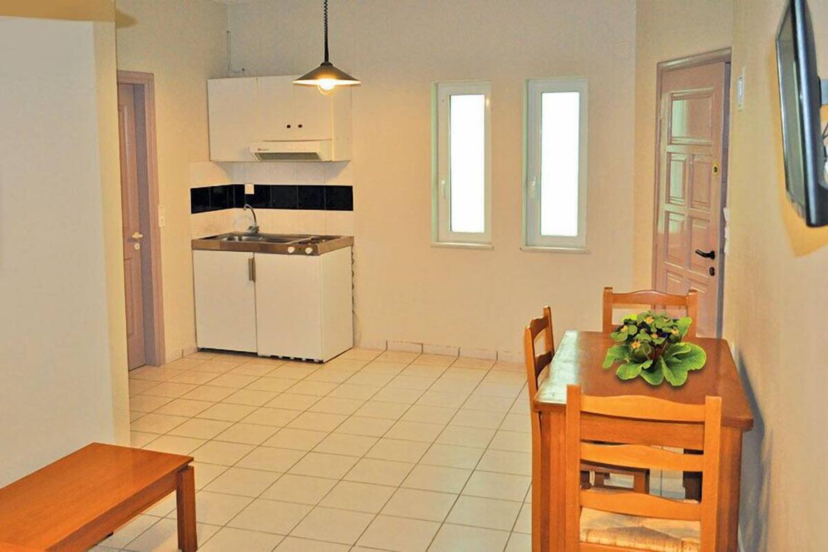 A compact kitchen with a stove, sink, and white cabinets, a dining area with a wooden table and chairs, and a small window.