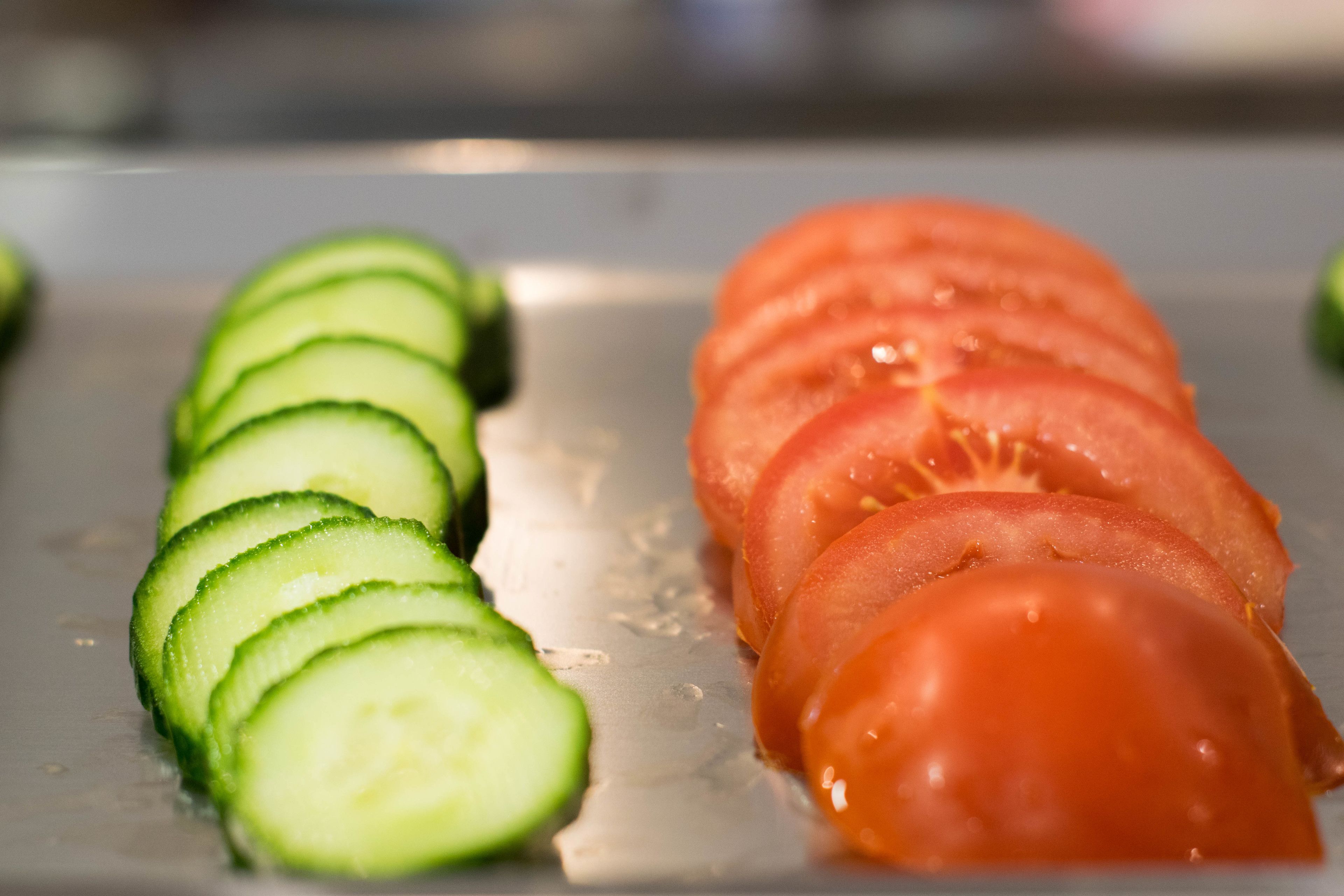 A kitchen counter with sliced cucumbers and tomatoes.